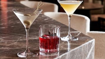 A bar area with a marble countertop, two martini glasses, and a small glass with a red drink.