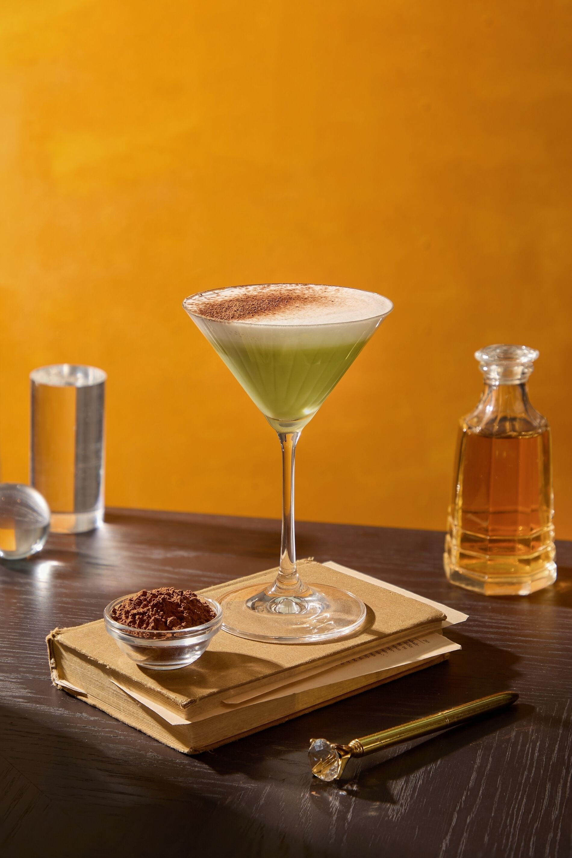 A martini glass with a green drink and a dusting of cocoa powder on a wooden table.