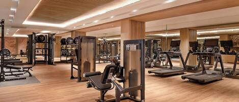 A modern gym with various exercise equipment, wooden flooring, and a spacious layout.