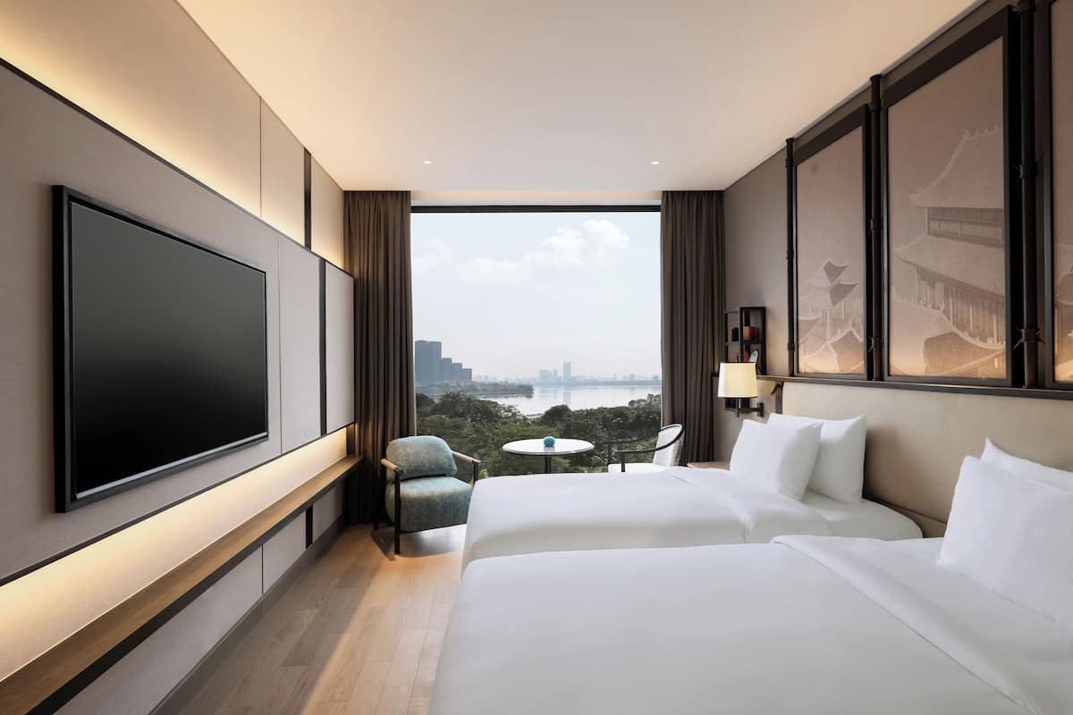Une chambre d’hôtel avec un grand lit, une télévision, une petite table et une vue sur le paysage urbain.