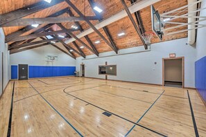 Uma quadra de basquete interna com piso de madeira, cesta de basquete e parede acolchoada azul.