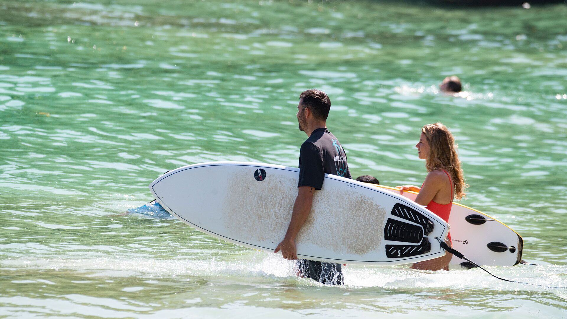 Un homme qui porte une planche de surf et une femme dans l’eau.
