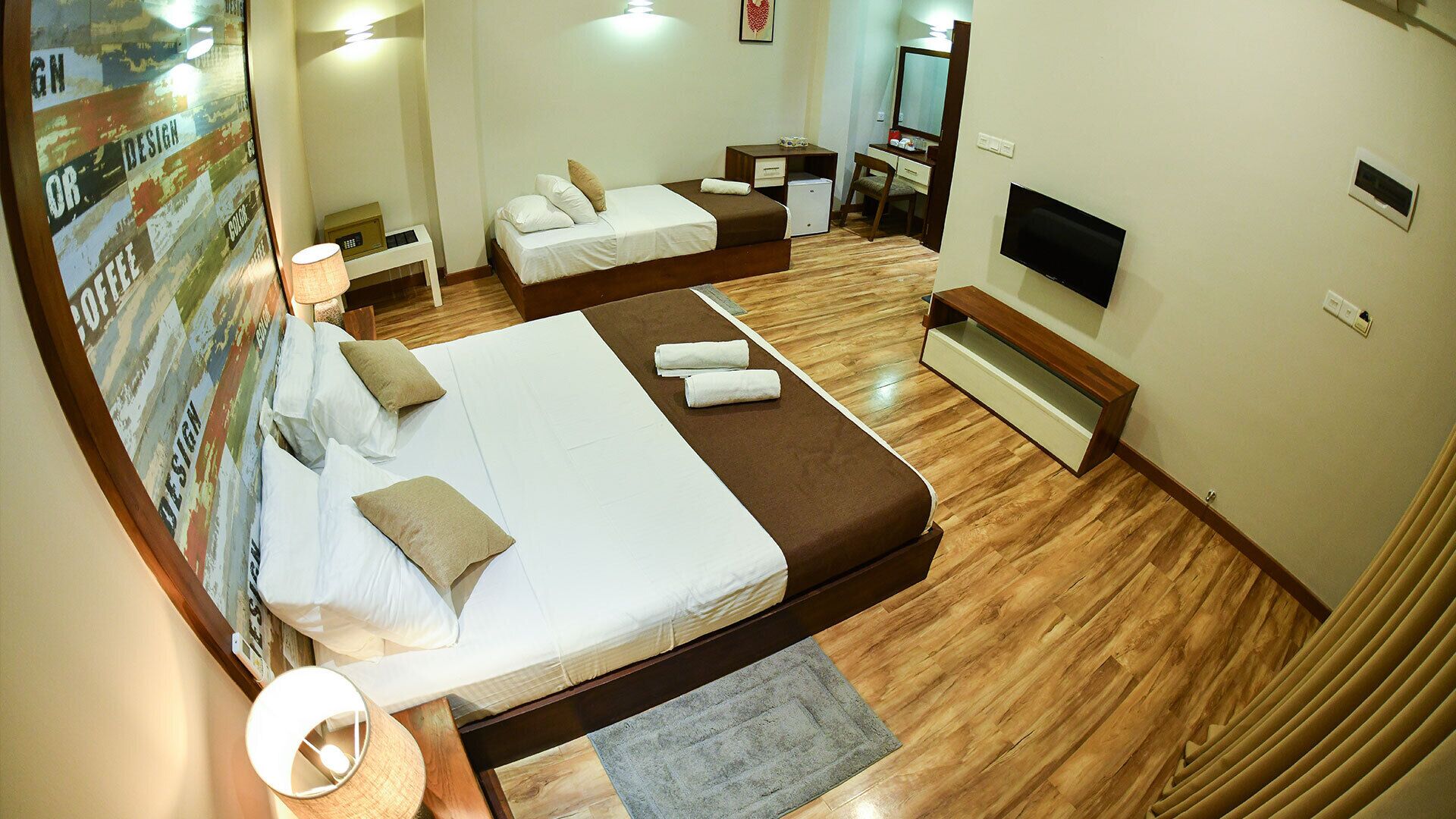A hotel room with a large bed, a desk, a chair, a TV, and a poster on the wall.