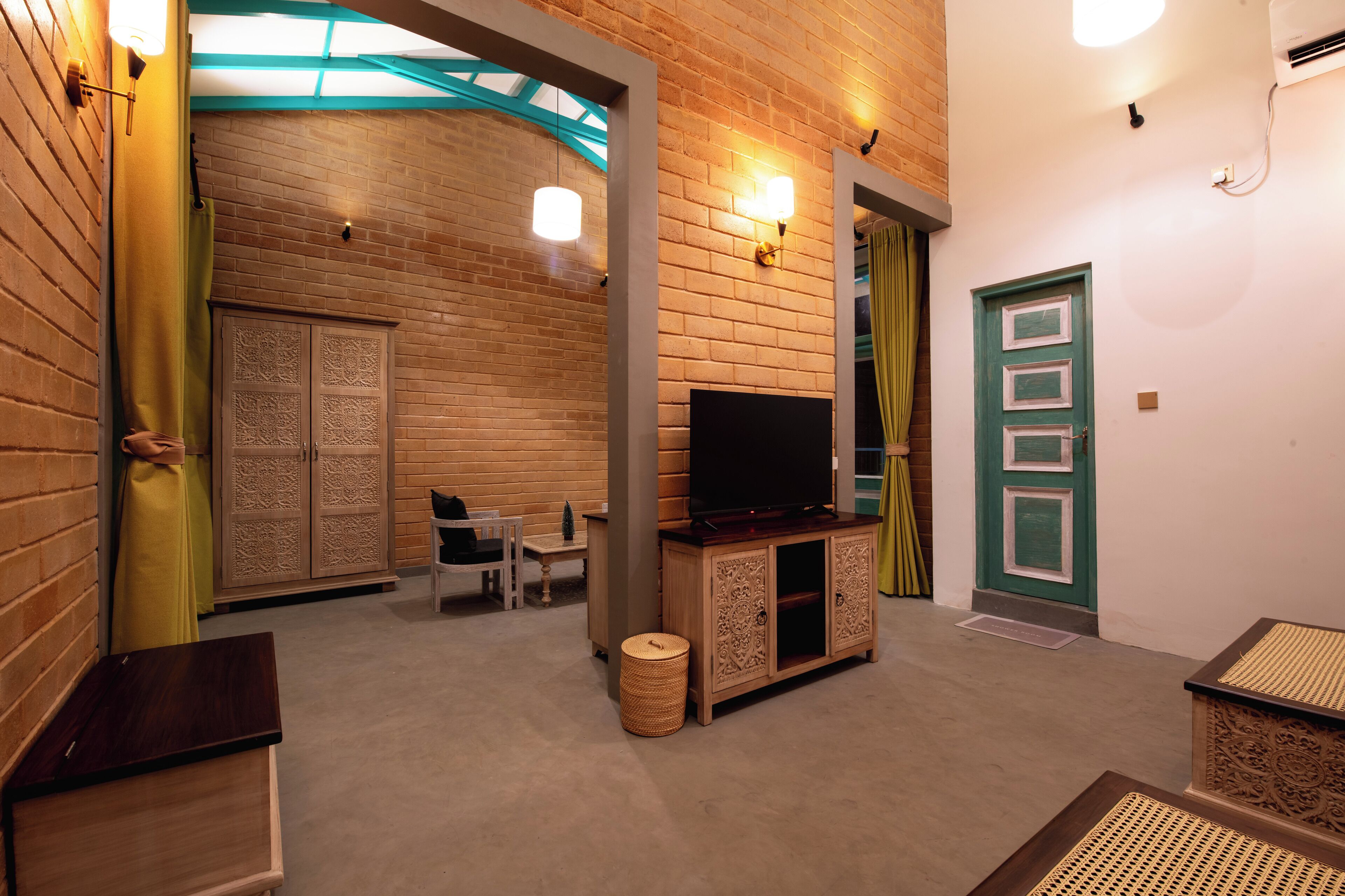 A room with a brick wall, a wooden cabinet with a television, a wicker basket, and a green door.
