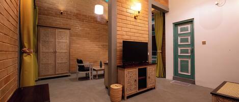 A room with a brick wall, a wooden cabinet with a television, a wicker basket, and a green door.