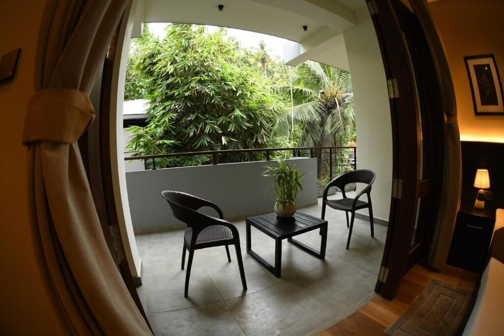 A balcony with two chairs and a table, a potted plant, and a view of lush greenery.