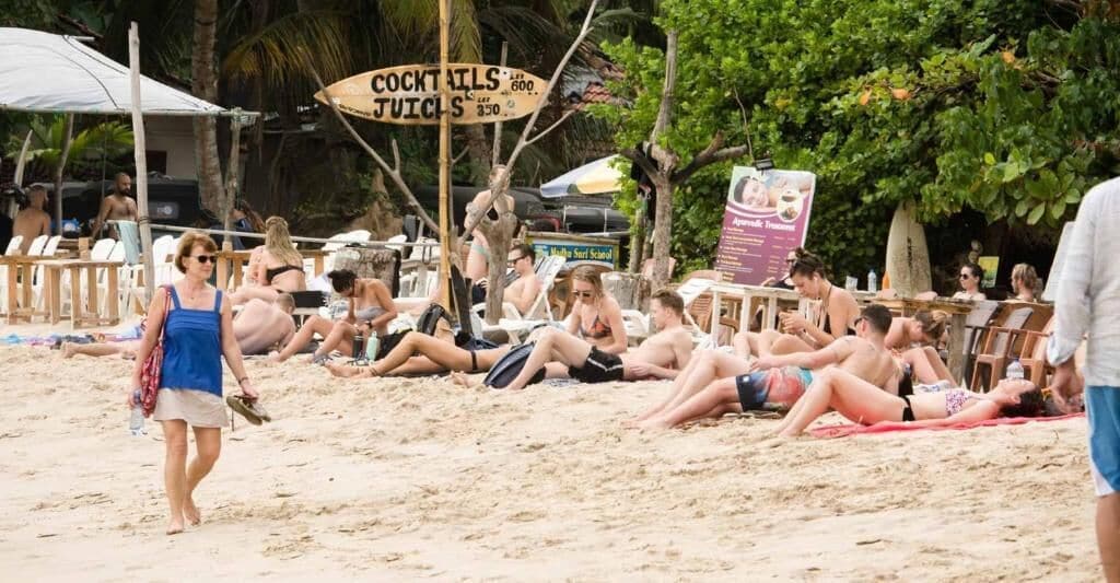 A beach scene with people sunbathing and a sign for 'COCKTAILS & JUICES'.