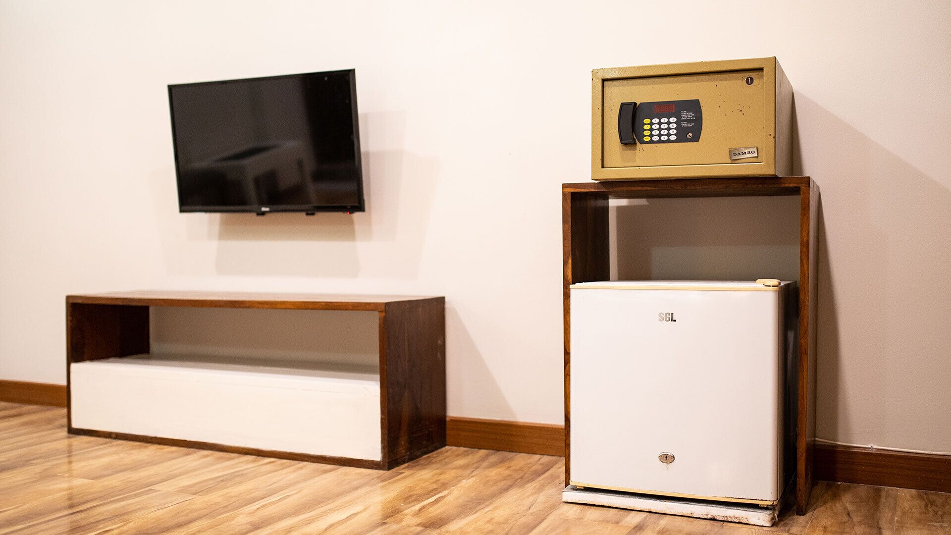 A room with a white refrigerator, a wooden cabinet, and a television mounted on the wall.