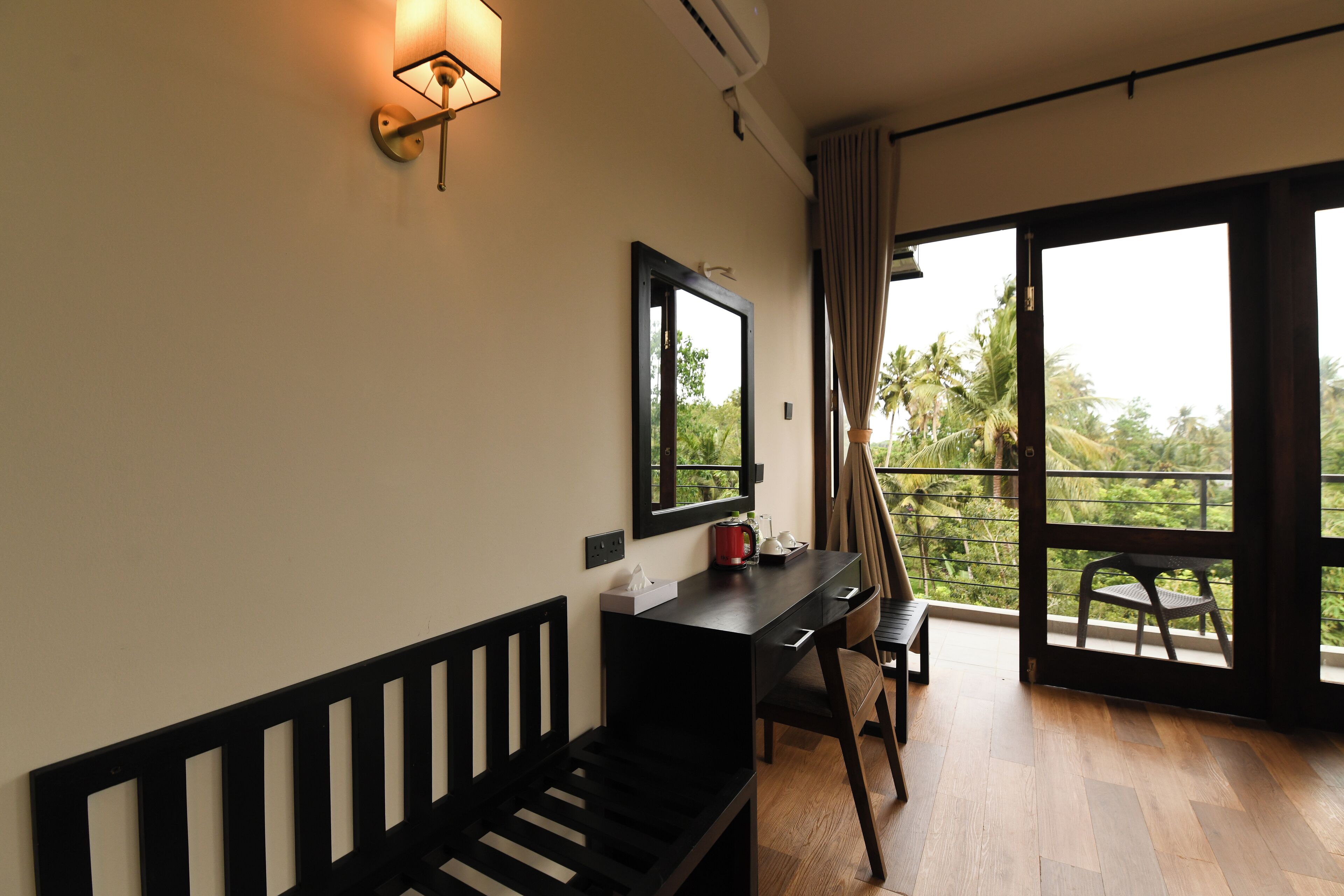 A room with a wooden bench, a desk, a chair, a mirror, and a window with a view of greenery.