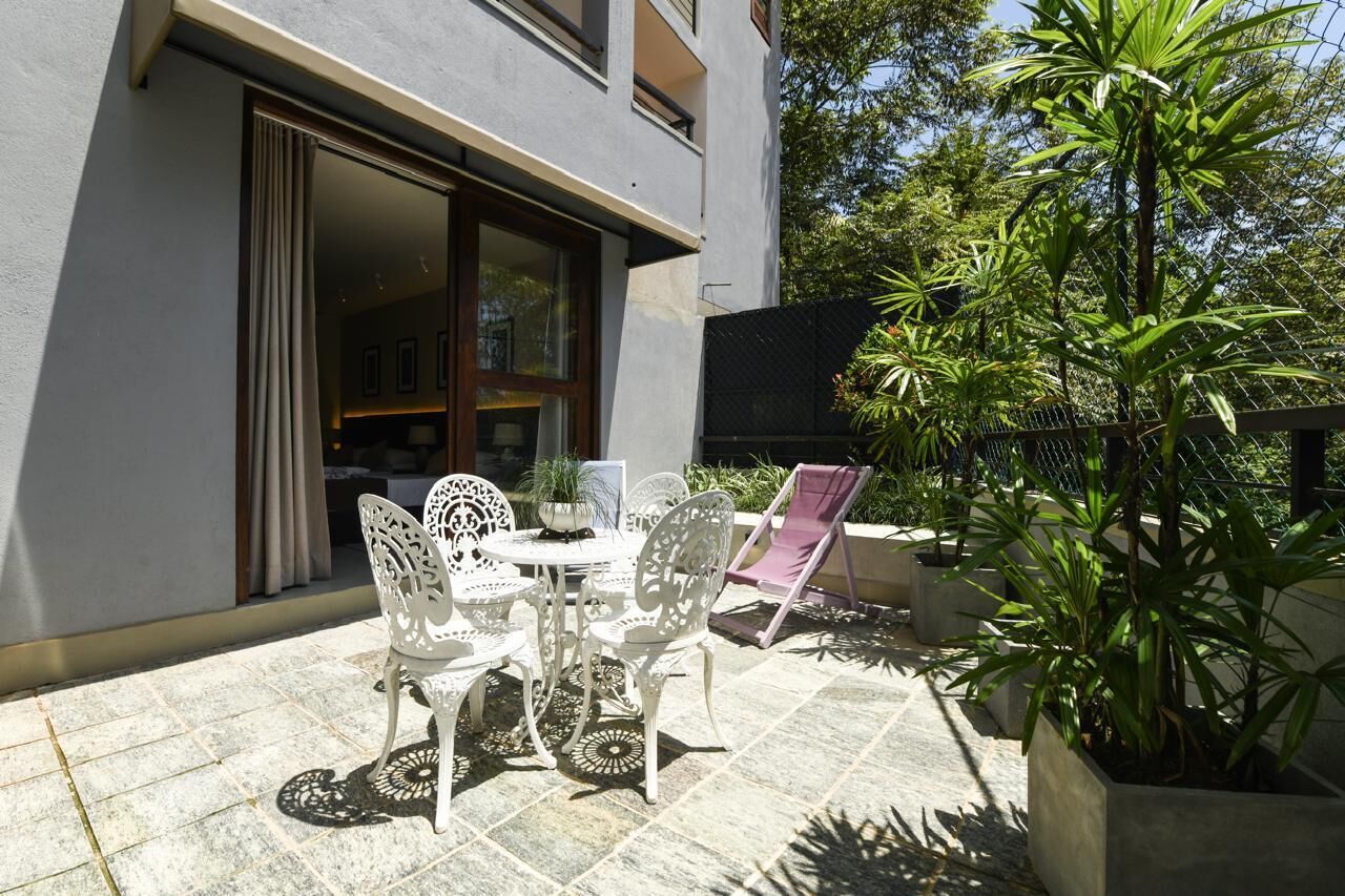 An outdoor patio with a table and chairs, surrounded by potted plants and a fence.