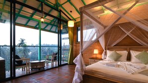 Une chambre à coucher comprenant un lit, une table de chevet, une lampe, une chaise, une petite table ronde et une vue sur l’extérieur grâce à de grandes fenêtres.