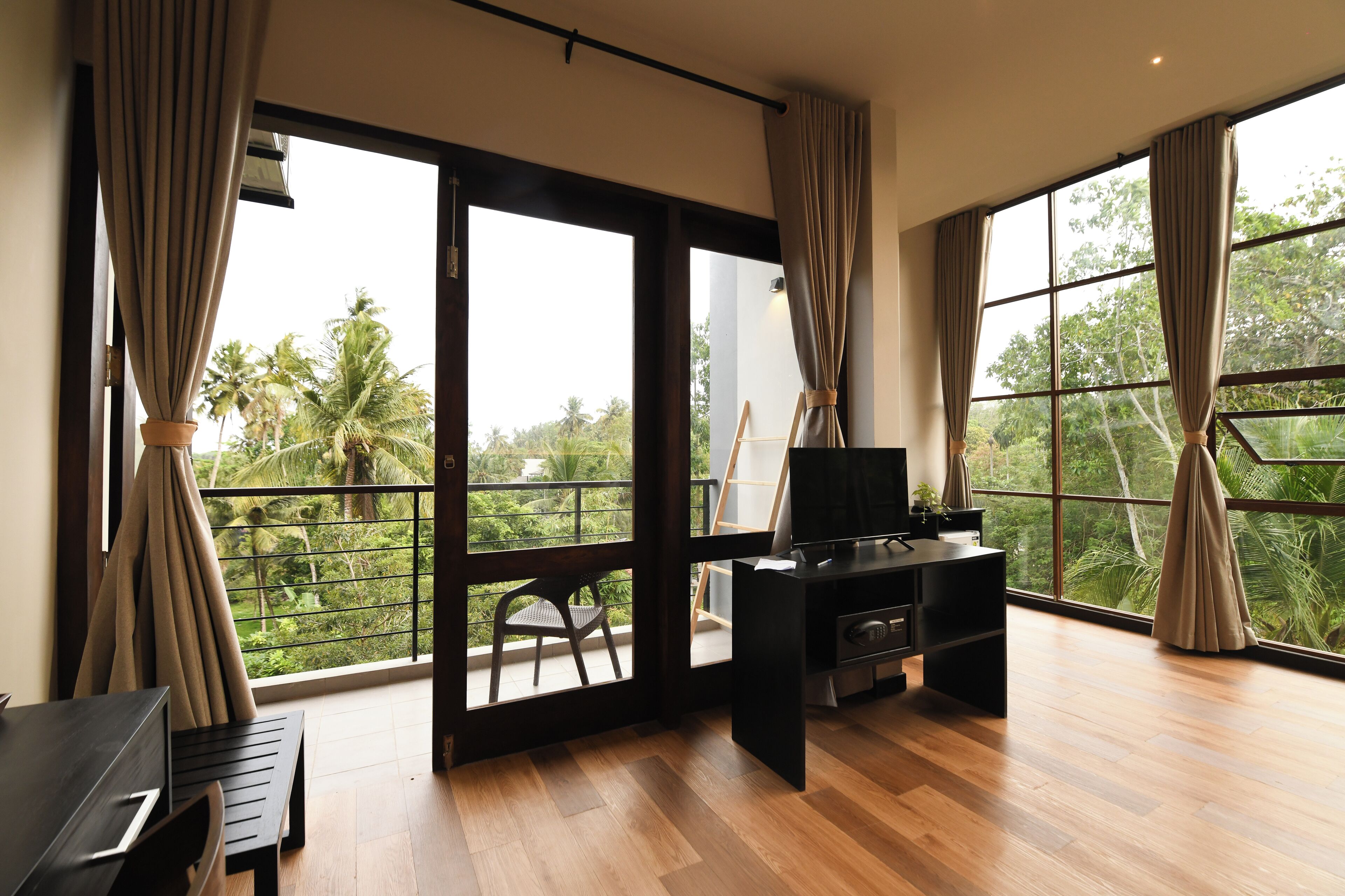 A spacious room with a large sliding glass door leading to a balcony, a black entertainment unit, and a wooden floor.