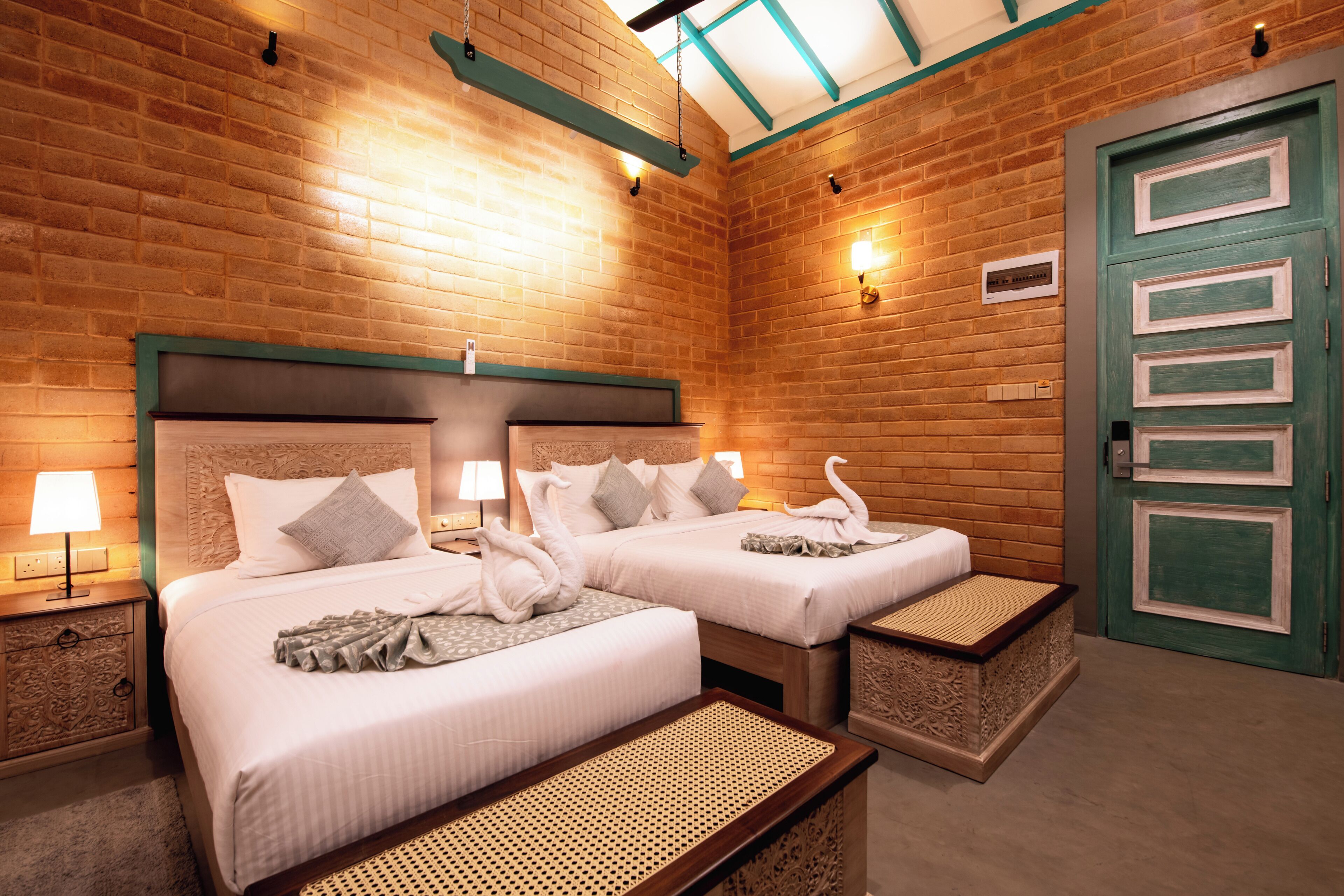 A hotel room with two beds, a green door, and a brick wall.