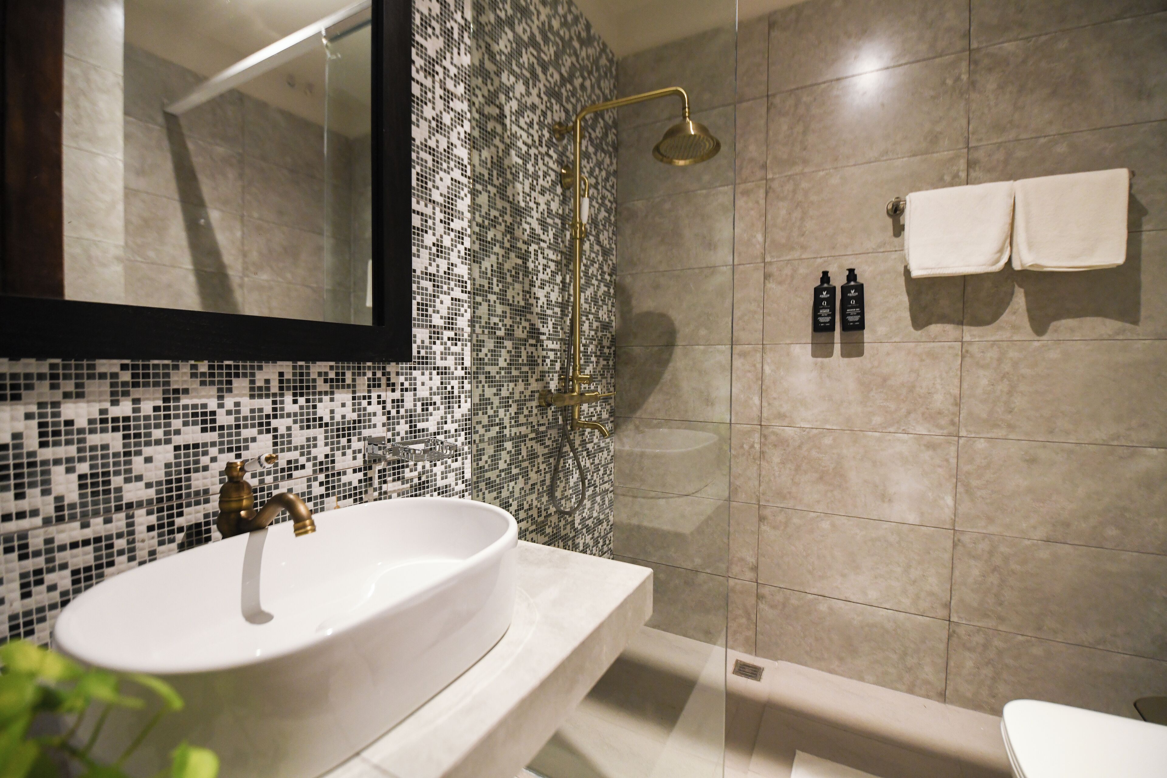 A bathroom with a white sink, a shower with a gold showerhead, and a tiled wall.