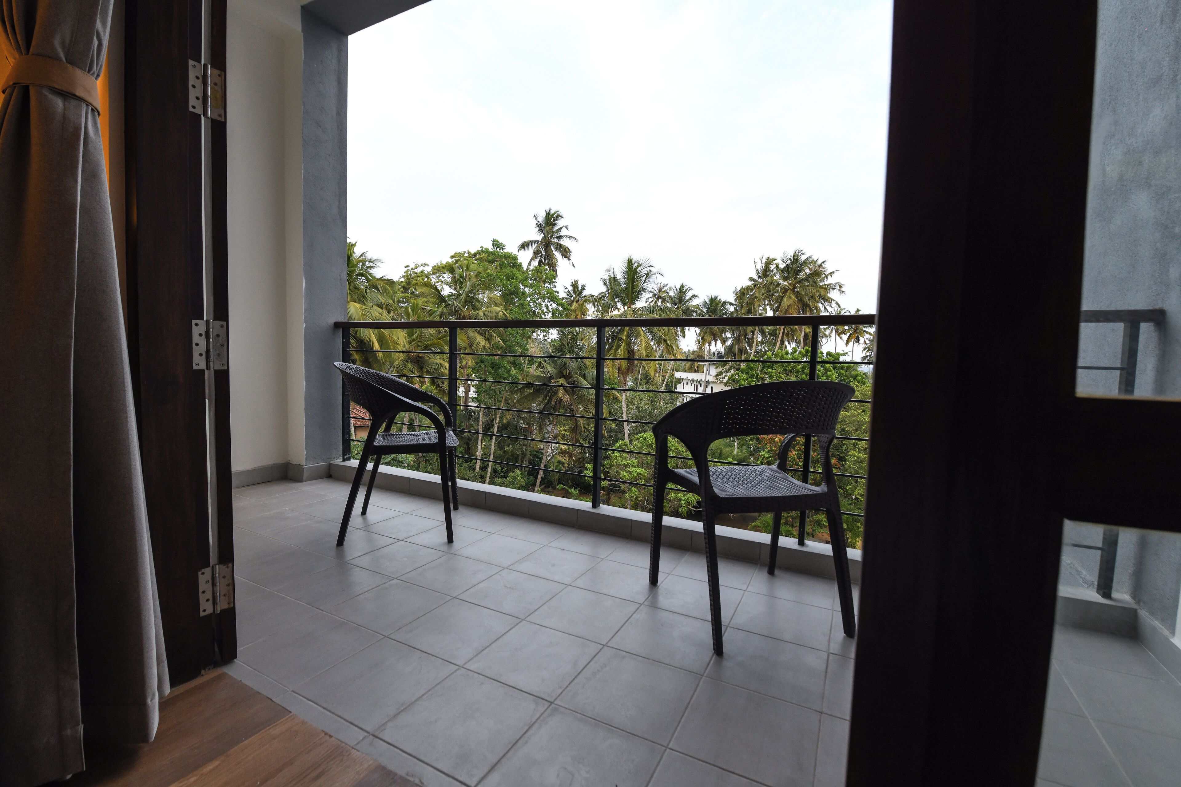 A balcony with two chairs, a view of palm trees, and a tiled floor.