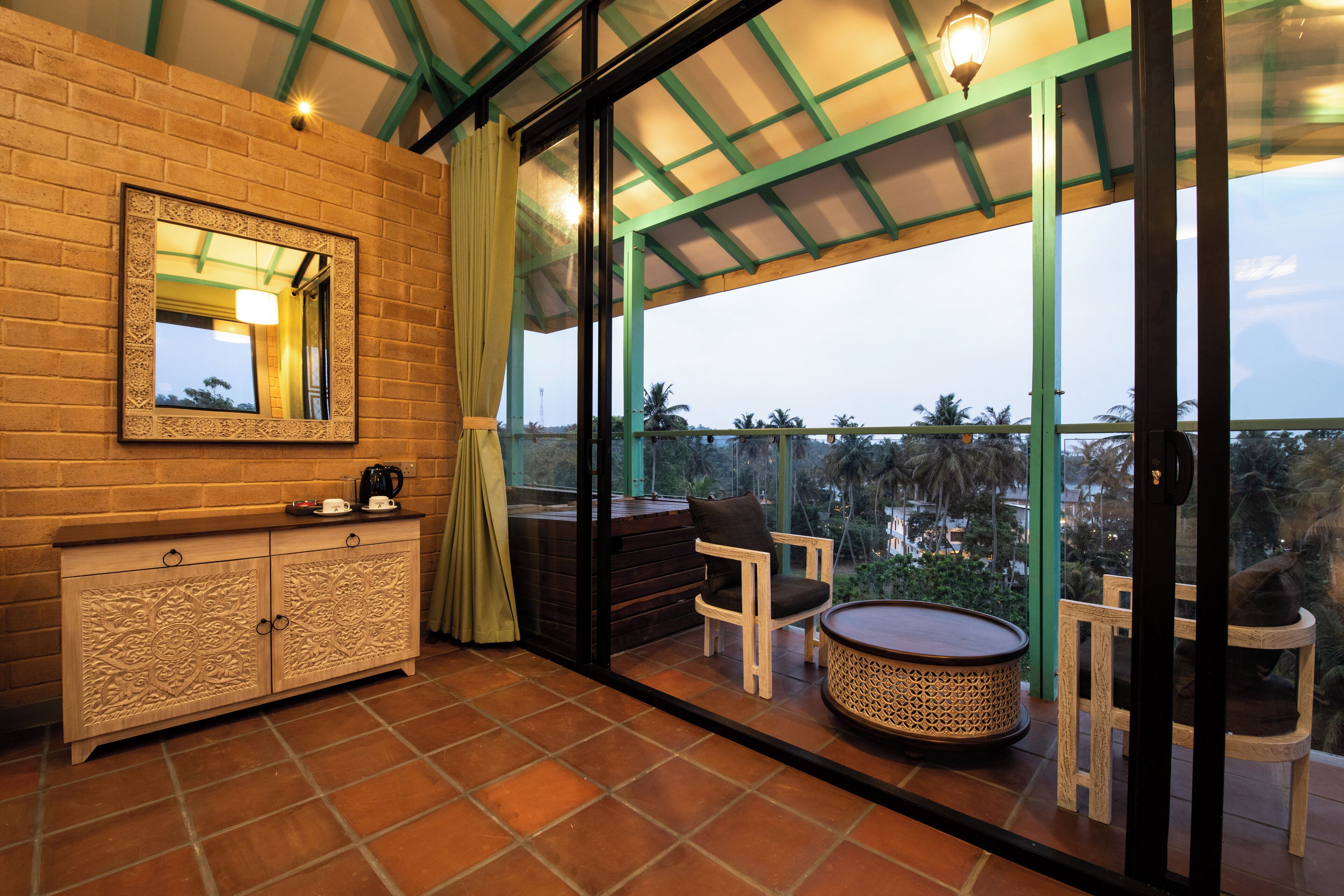 Un balcón con vista a palmeras, una silla de madera, una mesa redonda y un aparador con cajones.