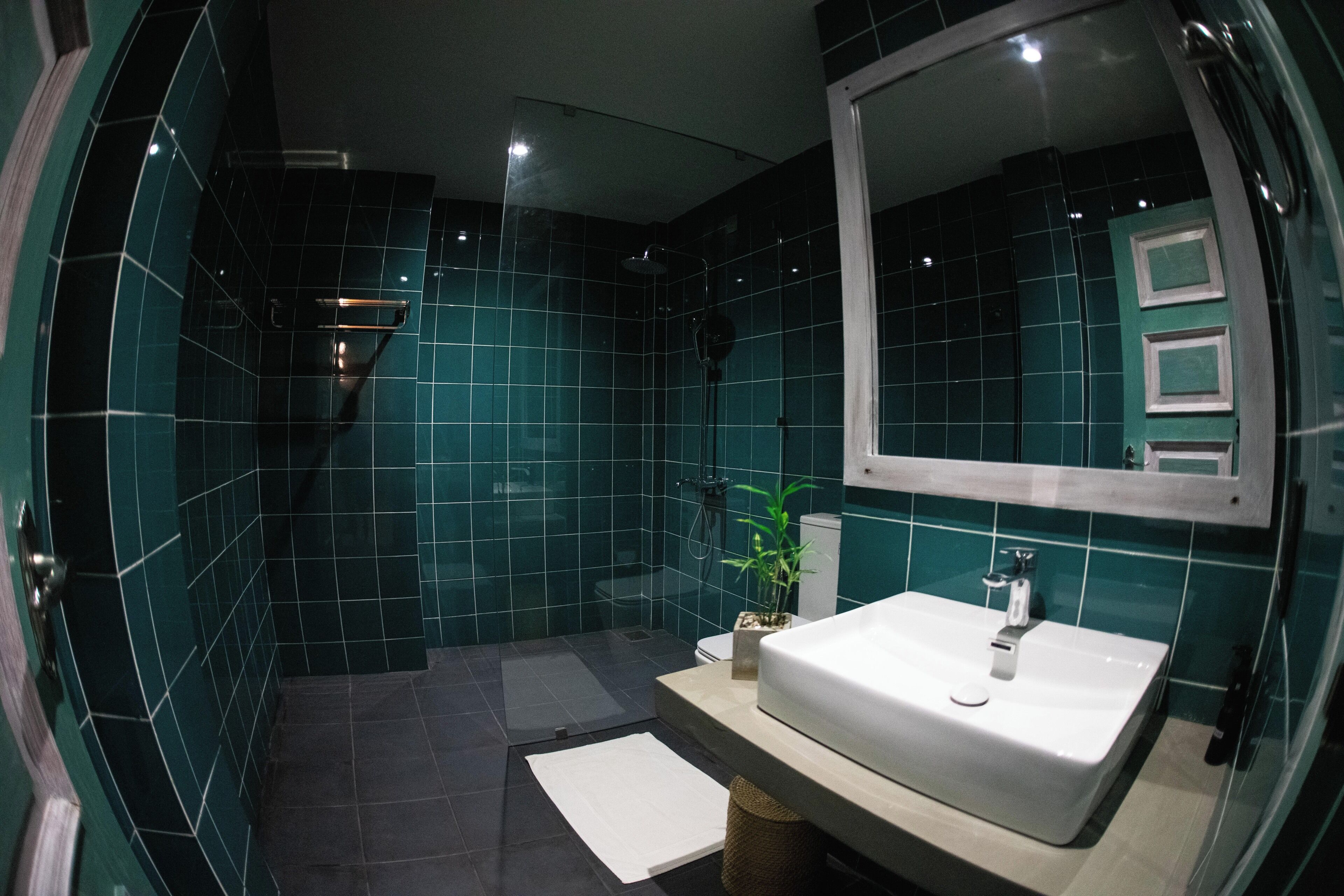 A bathroom with dark green tiles, a white sink, and a mirror above it.