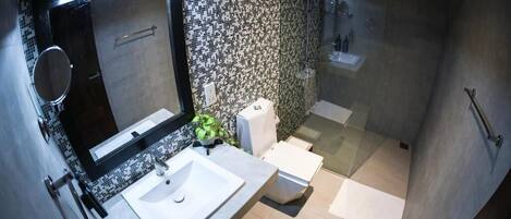 Un baño moderno con un espejo grande, lavamanos blanco y cabina de ducha con paredes de vidrio.