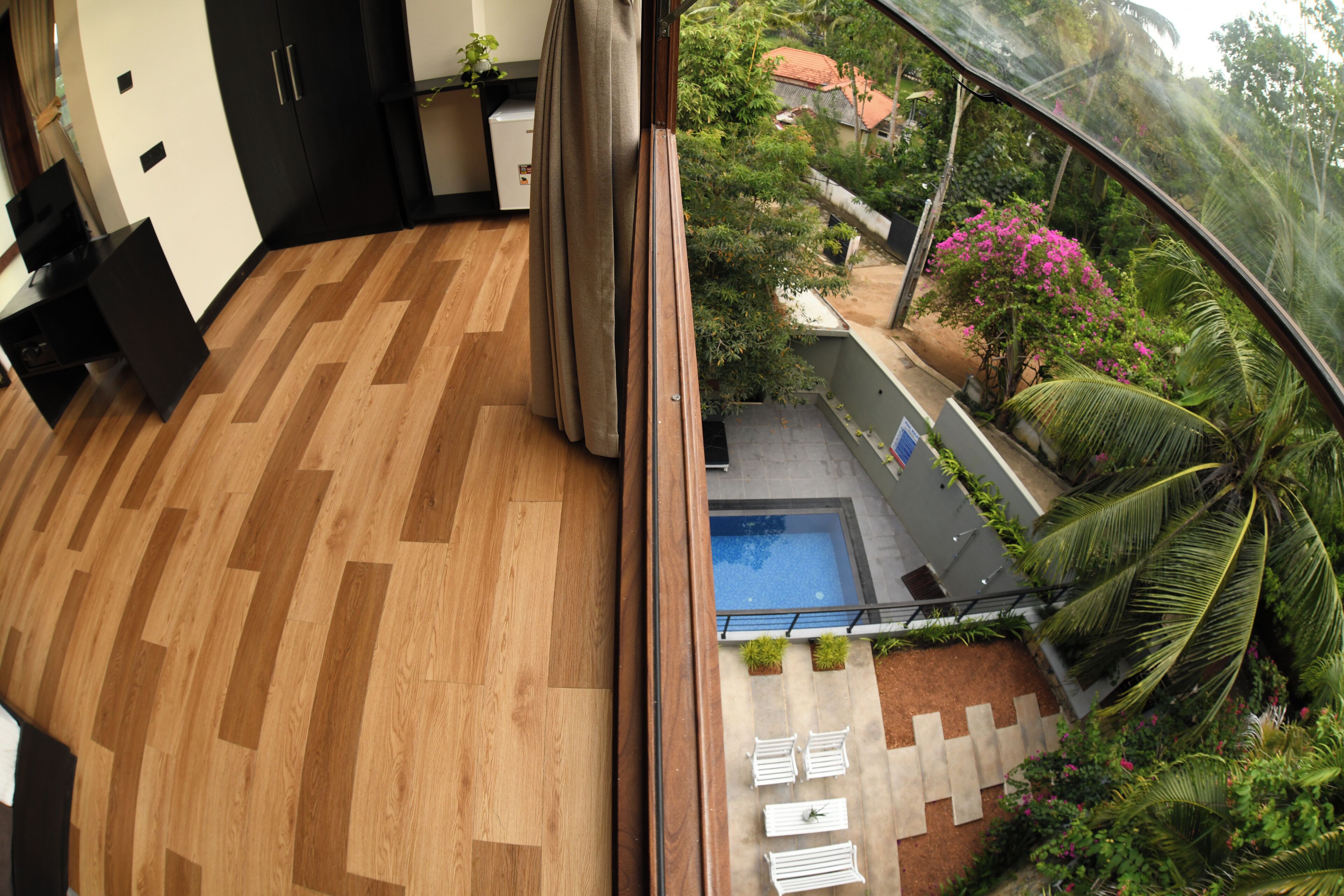 Una habitación moderna con suelo de madera, un ventanal y vistas a una piscina y follaje exterior.