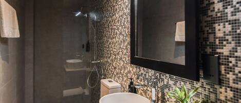 Un baño moderno con un espejo grande, un lavamanos sobre encimera y una zona de ducha.