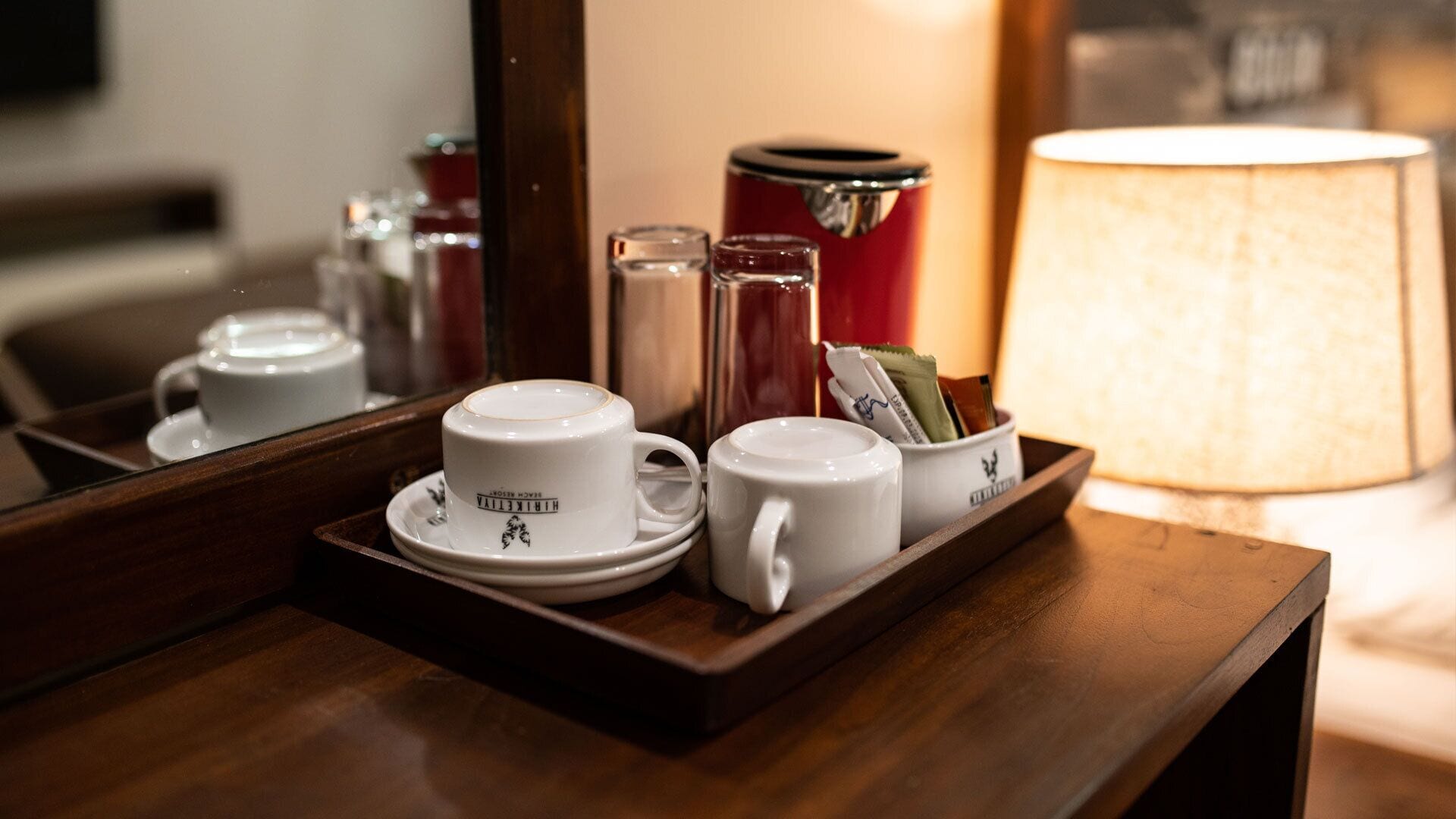 A tray with white cups and saucers, a red container, and a white mug on a wooden surface.