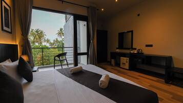 A hotel room with a large bed, a desk, a chair, and a balcony with a view of palm trees.