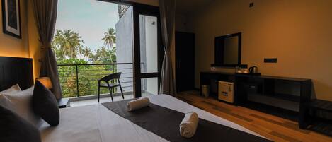 Habitación de hotel con una cama grande, un escritorio, una silla y un balcón con vistas a palmeras.