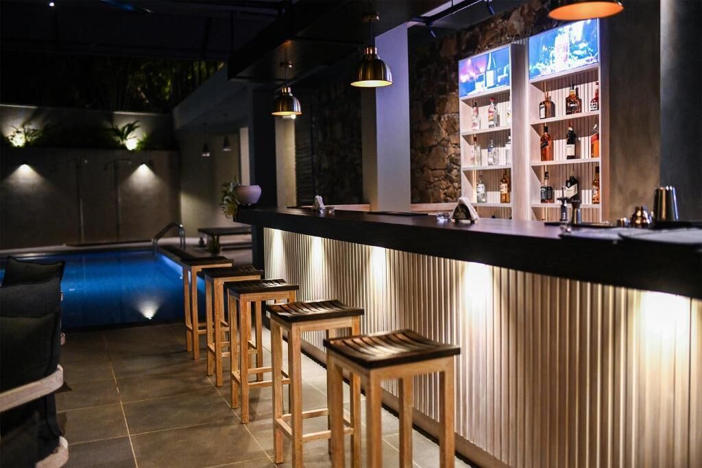 A bar area with wooden stools, a counter with a lighted display, and a pool in the background.
