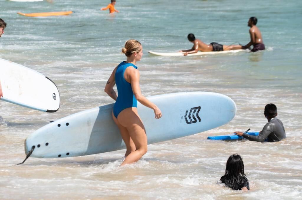 Eine Strandansicht mit Menschen im Wasser und auf Surfbrettern.