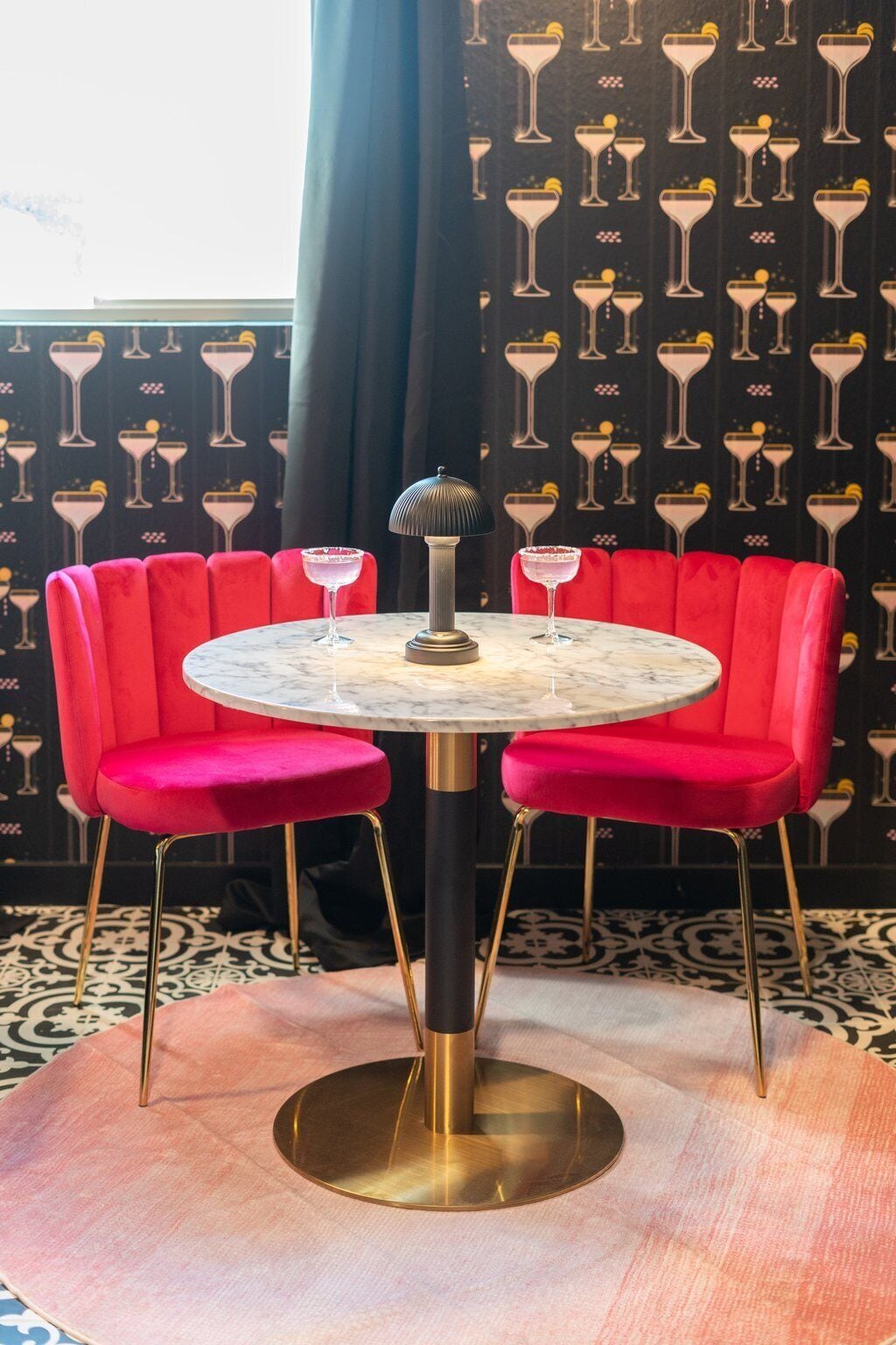 Une table ronde avec un plateau en marbre, deux chaises rouges à revêtement rembourré et une lampe noire.