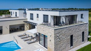 Een modern huis met een zwembad, een jacuzzi en een terras met loungestoelen.