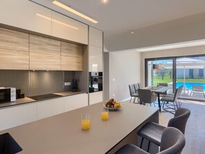 Eine moderne Küche mit einer großen Kochinsel, einem Essbereich mit Blick auf einen Pool und einem minimalistischen Design.