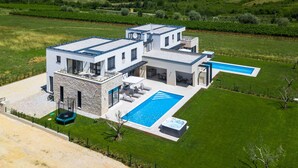 Una casa moderna de dos pisos con piscina, fachada de piedra y vistas al campo circundante.