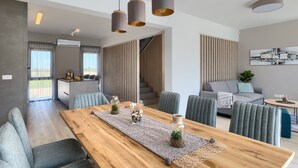 Un espacio habitable moderno con una mesa de comedor de madera, sillas tapizadas en gris e iluminación colgante.