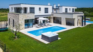 Una casa moderna de dos pisos con piscina, mobiliario exterior y bañera de hidromasaje.