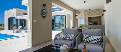 A modern living room with a pool view, a dartboard, and a dining area with a stone fireplace.