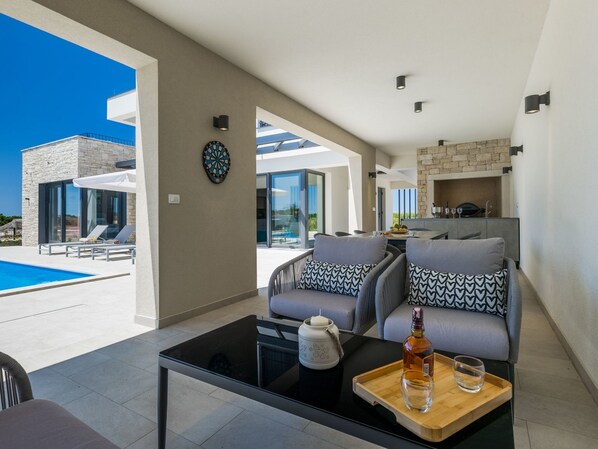 A modern living room with a pool view, a dartboard, and a dining area with a stone fireplace.