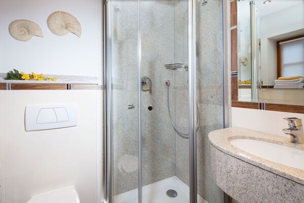 Une salle de bain moderne avec une douche à parois de verre, un lavabo sur un plan de travail en granit et des toilettes blanches.