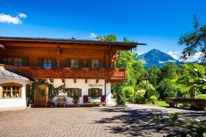 Un bâtiment traditionnel en bois, doté d’un balcon, d’une cour pavée et surplombant un paysage montagneux.