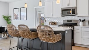 A modern kitchen with white cabinets, a central island with bar stools, a microwave, and a stove.
