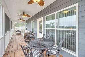 A covered porch with a round metal table and chairs, a sofa, and ceiling fans. - Dock & Fire Pit: Waterfront Midway Retreat! (Midway)