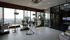 A modern hotel room with large windows, a dining area, and a view of the city. - Luxury Astra Sky River Apartment (Chang Wat Chiang Mai)