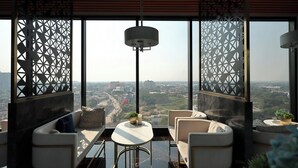A modern lounge with a city view, featuring a sofa, armchairs, a small table, and decorative plants. - Luxury Astra Sky River Apartment (Chang Wat Chiang Mai)
