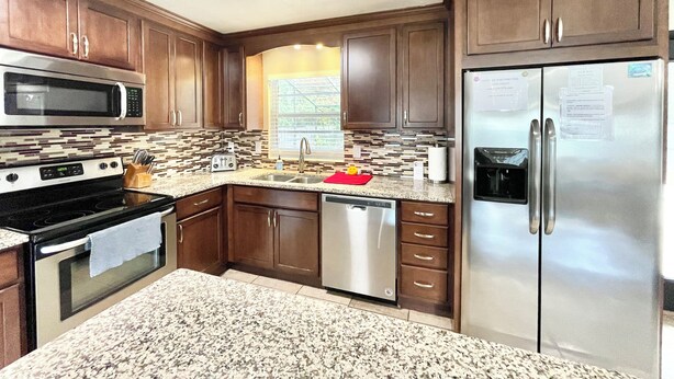 A kitchen with wooden cabinets, a stainless steel refrigerator, a microwave, an oven, and a dishwasher. - Spacious 4-bedroom house with Covered Private Pool in Gainesville (Gainesville)