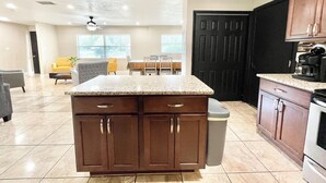 A kitchen with a granite countertop, wooden cabinets, a coffee maker, and a trash can. - Spacious 4-bedroom house with Covered Private Pool in Gainesville (Gainesville)