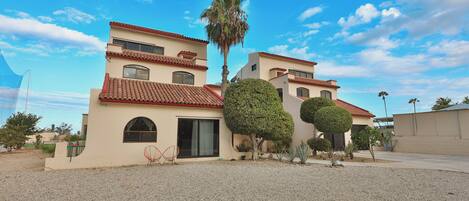 A two-story building with a red-tiled roof, a palm tree, and a well-maintained garden.