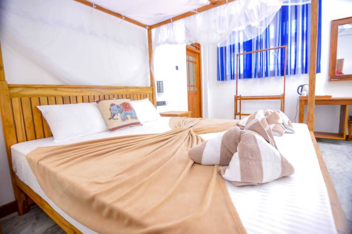 A neatly made bed with a beige blanket, a pillow with an elephant design, and a canopy overhead.