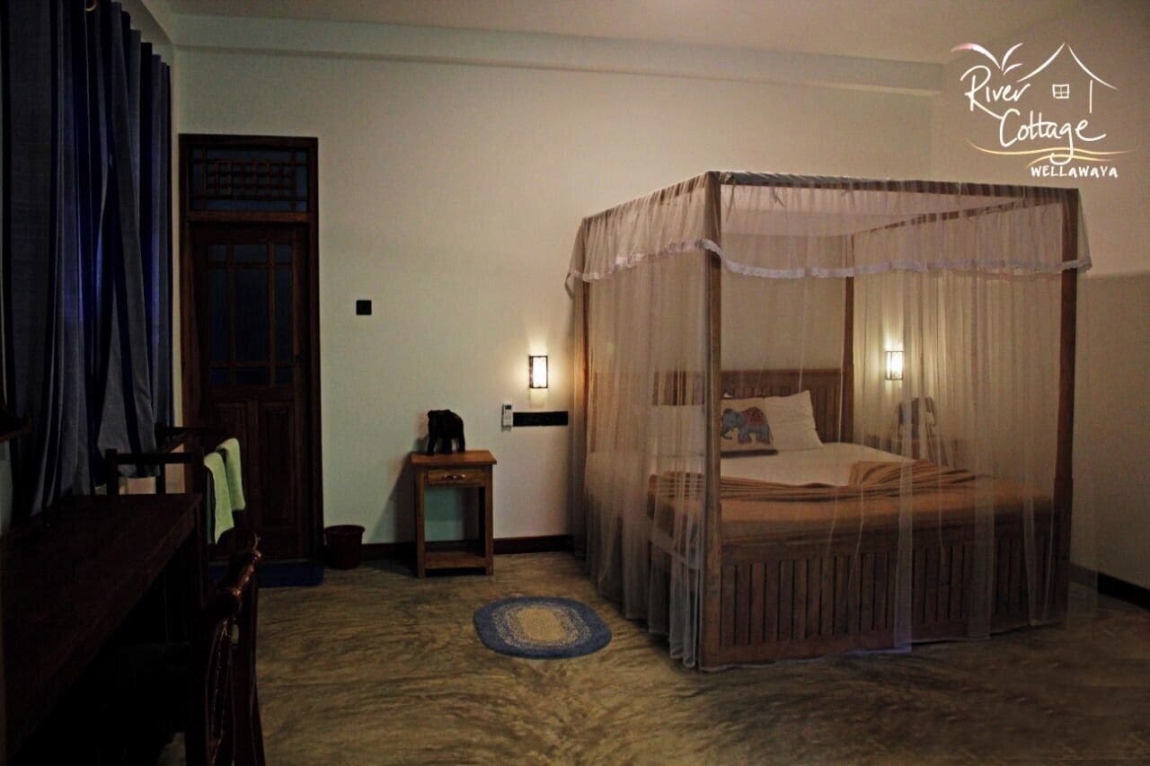 A room with a four-poster bed, a small table with a lamp, a chair, and a wooden door.