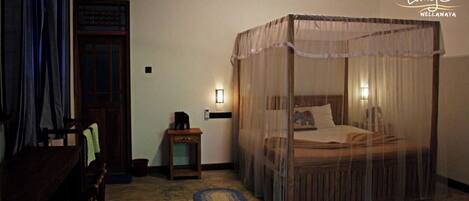 Una habitación con una cama con dosel, una mesita con lámpara, una silla y una puerta de madera.