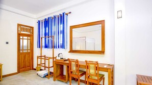 A room with a wooden desk, two chairs, a window with blue curtains, a wooden door, and a mirror on the wall. - River Cottage Wellawaya (Wellawaya)